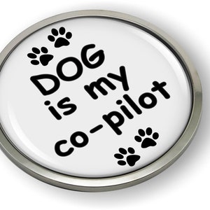 May include: A white round button with a silver metal rim. The button has black paw prints and the text "DOG is my co-pilot".