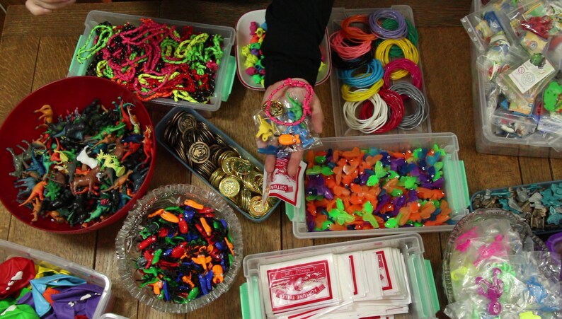 May include: Assortment of colorful plastic toys in clear containers, including dinosaurs, butterflies, and small figures. There are also gold coins, rubber bands, and a bag of small toys.