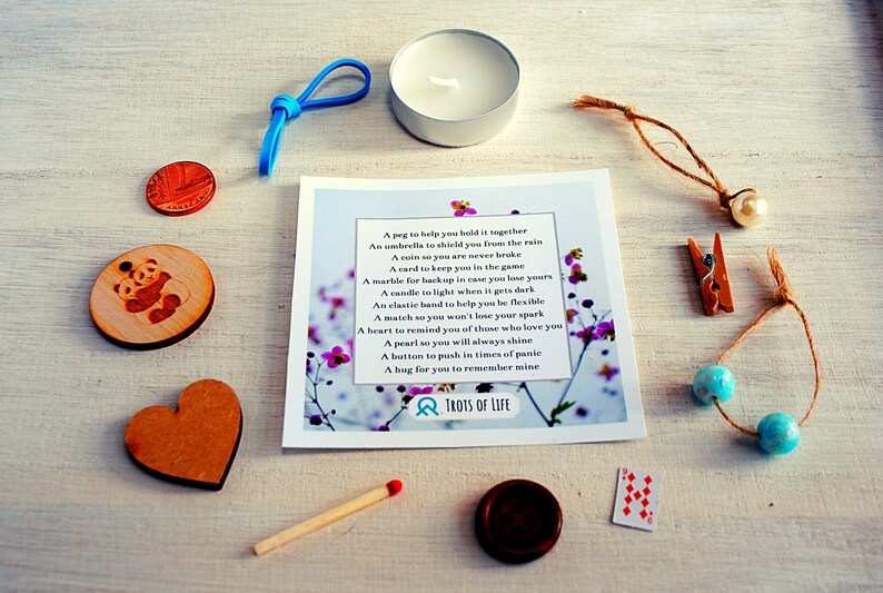 May include: A small gift box with a variety of items, including a wooden heart, a panda bear, a small candle, a match, a peg, a coin, a card, a marble, a clothespin, a pearl, beads, and a small card with a poem about the items. The poem reads: "A peg to help you hold it together, An umbrella to shield you from the rain, A coin so you are never broke, A card to keep you in the game, A marble for backup in case you lose yours, A candle to light when it gets dark, An elastic band to help you be flexible, A match so you won't lose your spark, A heart to remind you of those who love you, A pearl so you will always shine, A button to push in times of panic, A hug for you to remember mine." The card also has the text "TROTS OF LIFE" on it.