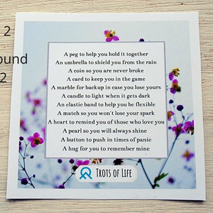 May include: A white card with a blue background and pink flowers. The card has a poem on it that reads: "A peg to help you hold it together, An umbrella to shield you from the rain, A coin so you are never broke, A card to keep you in the game, A marble for backup in case you lose yours, A candle to light when it gets dark, An elastic band to help you be flexible, A match so you won't lose your spark, A heart to remind you of those who love you, A pearl so you will always shine, A button to push in times of panic, A hug for you to remember mine." The card also has the text "TROTS OF LIFE" at the bottom.