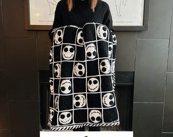 May include: A woman is holding a black and white crochet blanket with a pattern of Jack Skellington's face. The blanket is folded in half and the woman is holding it in front of her chest. The text "PDF file only" is visible in the bottom of the image.