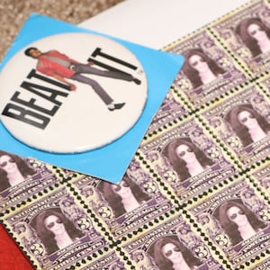 May include: A sheet of postage stamps featuring a woman with long dark hair and sunglasses. The stamps are arranged in a grid pattern and have a purple and yellow color scheme. The text "BEAT IT" is visible on a blue sticker in the upper left corner of the image.