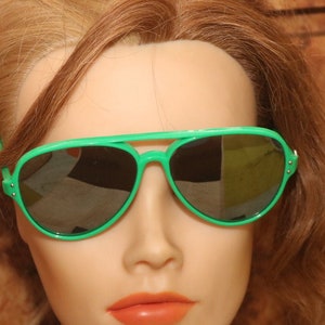 Puede incluir: Un maniquí con gafas de sol aviador verdes sobre un fondo de madera marrón.