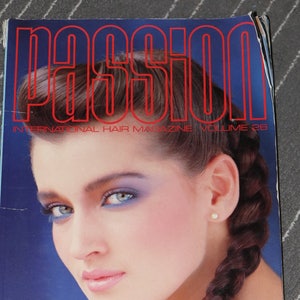 May include: A magazine cover featuring a woman with long brown hair styled in a braid. The magazine is titled "PASSION INTERNATIONAL HAIR MAGAZINE VOLUME 26" and features a Passion Exclusive with Michael, Paul Nat Hair Studio, and Sanrizz. The cover also includes a showcase with an interview with Llongueras.