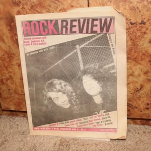 May include: A black and white magazine cover with the title "ROCK REVIEW" in pink letters. The cover features a photo of two people with long hair, and the text "Danzig at the Palace" and "We Keep the Rock in L.A." are visible.