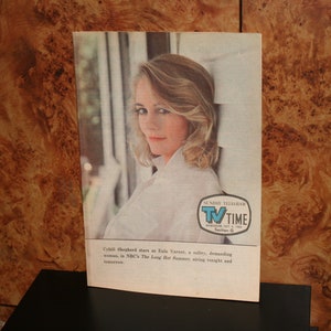 Op de afbeelding: Een zwart-witfoto van een vrouw met blond haar. Ze draagt een wit shirt en kijkt naar de camera. De foto is afkomstig uit een tijdschrift genaamd "TV TIME" en bevat de tekst "Cybill Shepherd stars as Ella Verne, a witty, demanding woman, in NBC's "The Long Hot Summer", airing tonight and tomorrow."
