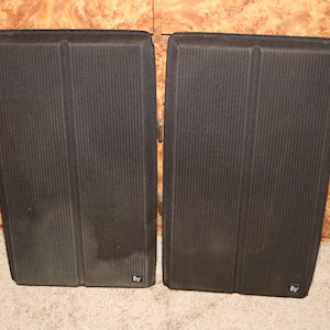 May include: A pair of black speaker cabinets with a ribbed texture and the text "EV" on the bottom right corner of each cabinet.