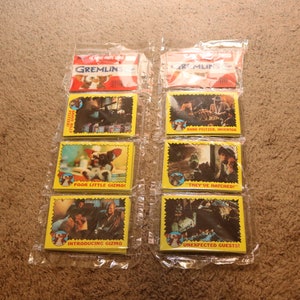 May include: A set of eight trading cards featuring images from the movie Gremlins. The cards are yellow with black text and feature images of the characters from the movie. The cards are in plastic sleeves.