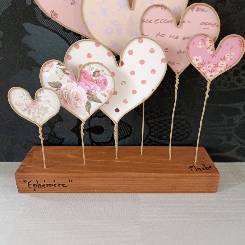 May include: A wooden base with the words "Ephemer" and "Plache" inscribed on it.  Five paper hearts with different patterns are attached to the base with twine.