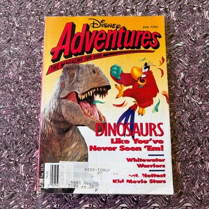 May include: A July 1993 issue of Disney Adventures magazine for kids featuring a large brown Tyrannosaurus Rex on the left and a red parrot character on the right. The cover text reads Disney Adventures, Dinosaurs Like You've Never Seen 'Em, Whitewater Warriors, and Hottest Kid Movie Stars.