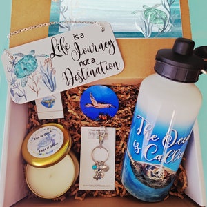 May include: A gift box filled with sea-themed items, including a candle, a water bottle, a keychain, and a sign that reads "Life is a Journey not a Destination".