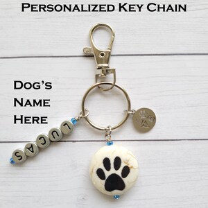 May include: Personalized silver key chain with a silver charm that says "Pawsitive" and a white ceramic charm with a black paw print. The key chain also has silver beads that spell out the name "Lucas".