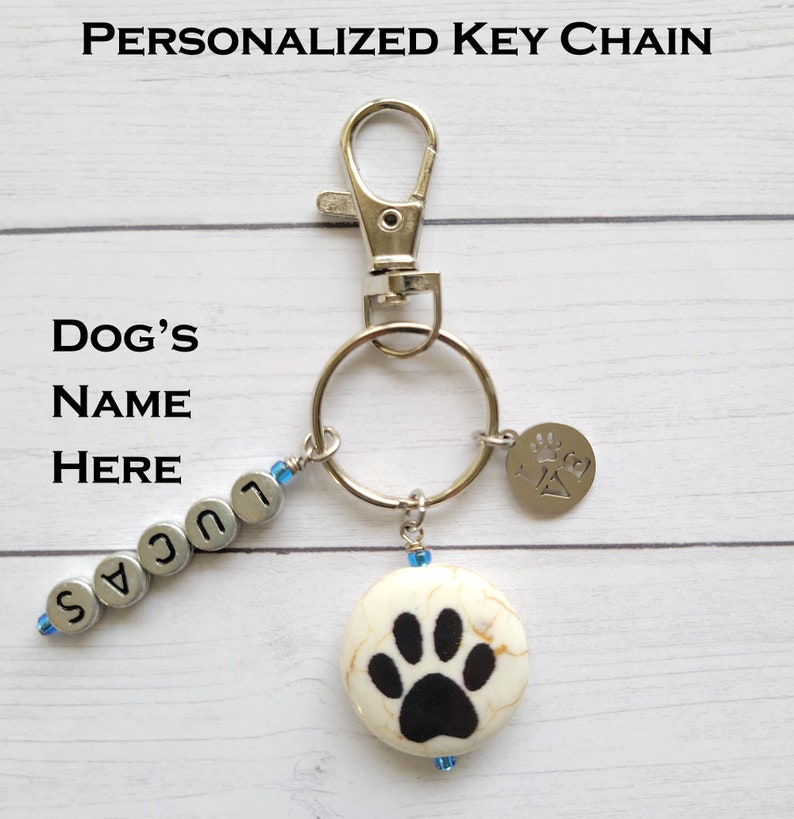 May include: Personalized silver key chain with a silver charm that says "Pawsitive" and a white ceramic charm with a black paw print. The key chain also has silver beads that spell out the name "Lucas".