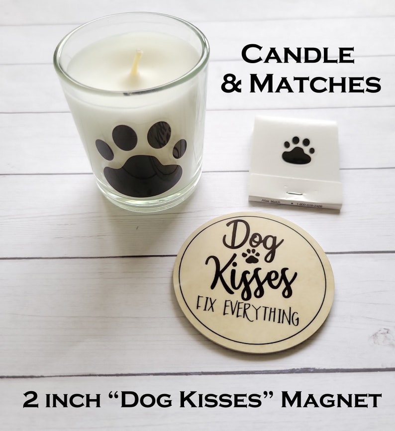May include: A white candle with a black paw print design in a glass jar, a pack of matches with a paw print design, and a 2 inch round wooden magnet with the text "Dog Kisses Fix Everything" and a paw print.