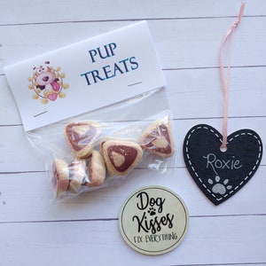 May include: A bag of pink and white heart-shaped dog treats with a label that says "Pup Treats". There is a black heart-shaped tag with the name "Roxie" written on it and a round sticker that says "Dog Kisses Fix Everything".