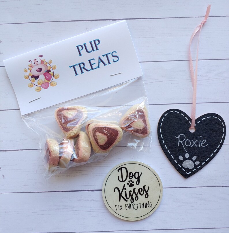 May include: A bag of pink and white heart-shaped dog treats with a label that says "Pup Treats". There is a black heart-shaped tag with the name "Roxie" written on it and a round sticker that says "Dog Kisses Fix Everything".