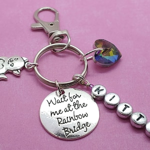 May include: Silver keychain with a cat charm, a heart charm, a rainbow bridge charm, and a crystal heart charm. The keychain also has a charm with the word "Kitty" spelled out in silver beads.