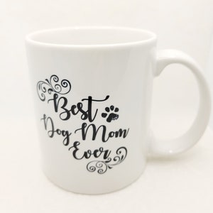May include: White ceramic coffee mug with black text that reads "Best Dog Mom Ever" with a paw print graphic and decorative swirls.