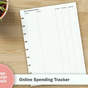 May include: A white planner sheet with the text "Online Purchases Tracker" and "Online Spending Tracker" on a wooden surface. The sheet has pre-printed lines for tracking purchases. A small potted plant and a box of colored pencils are also visible.