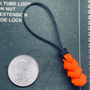 May include: A small orange and black paracord keychain with a loop at the top. The keychain is about the size of a US quarter.