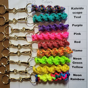 May include: A set of 10 keychains with different colored paracord. The paracord is woven in a braided pattern. The keychains are attached to gold metal key rings. The colors of the paracord are: Kaleidoscope, Teal, Purple, Pink, Red, Flame, Neon Green, Yellow, Neon Rainbow.