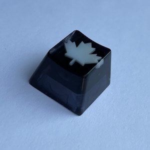 May include: Black keycap with a white maple leaf design.