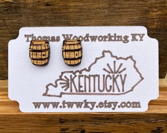 May include: A pair of wooden earrings shaped like miniature barrels. The earrings are on a white card with the text "Thomas Woodworking KY" and an outline of the state of Kentucky with the word "KENTUCKY" inside. The card also has the website address "www.twwky.etsy.com".