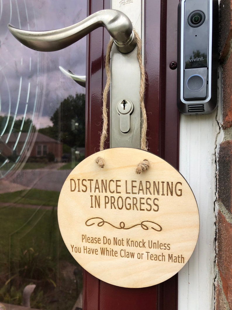 May include: A wooden sign with the text "Distance Learning in Progress" and the message "Please Do Not Knock Unless You Have White Claw or Teach Math".