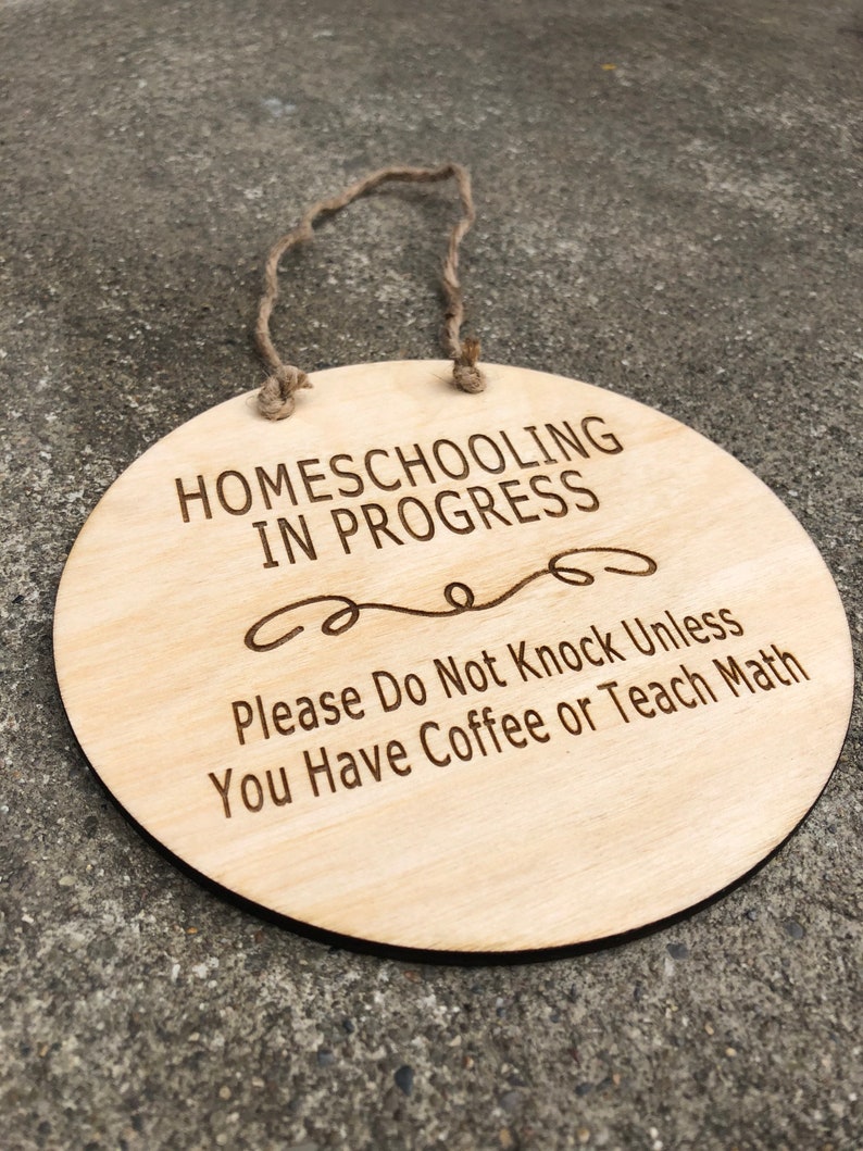 May include: A round wooden sign with a rope hanger reads "Homeschooling in Progress. Please Do Not Knock Unless You Have Coffee or Teach Math."