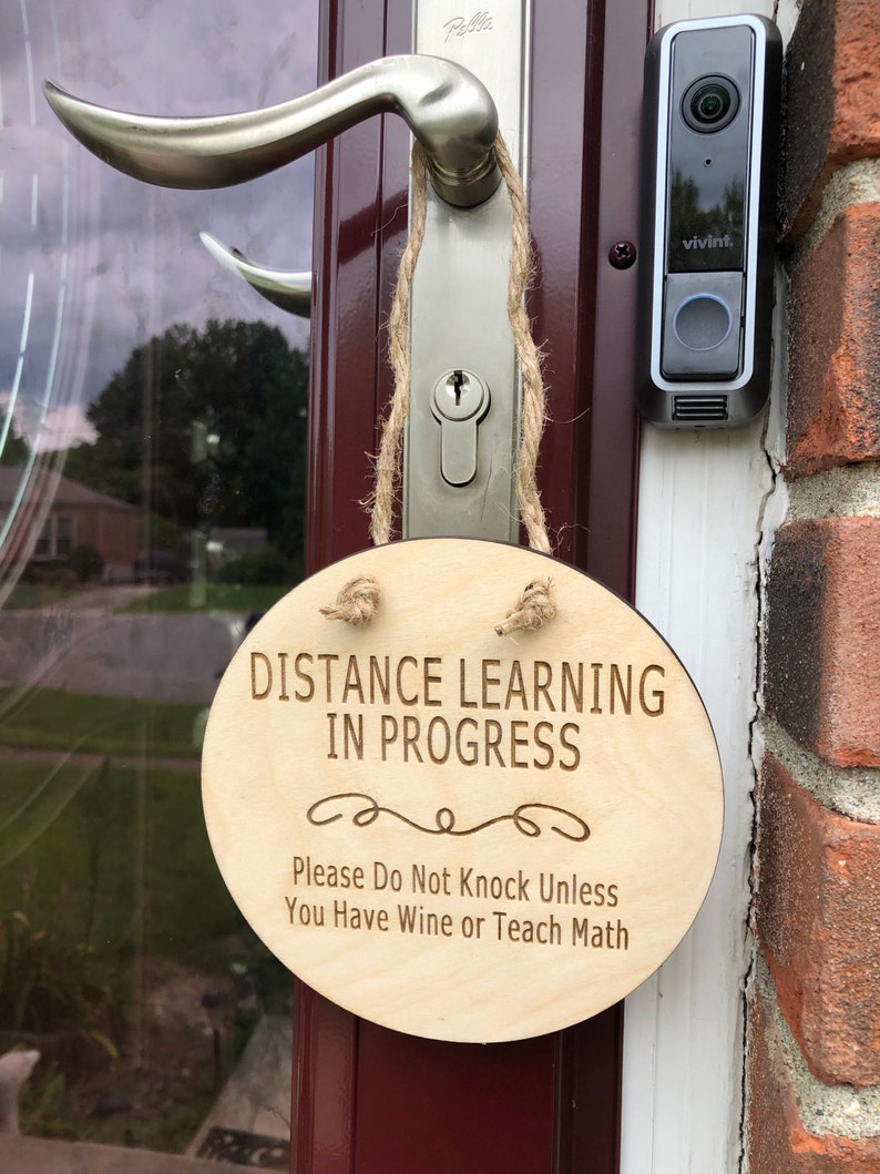May include: A round wooden sign with the text "Distance Learning in Progress" and the message "Please Do Not Knock Unless You Have Wine or Teach Math".