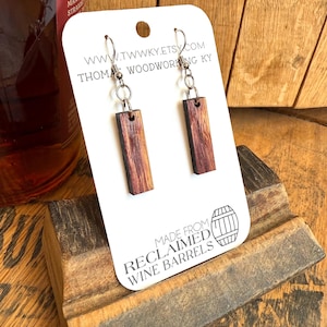 May include: A pair of wooden earrings made from reclaimed wine barrels. The earrings are brown and have a natural wood finish. The earrings are hanging on a white card with the text "www.twvky.etsy.com Thomas Woodworking KY" and "Made from Reclaimed Wine Barrels".