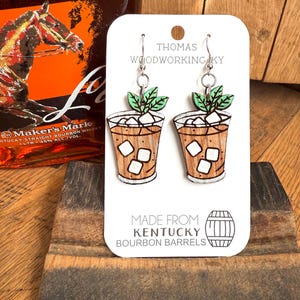 May include: A pair of wooden earrings shaped like a glass of iced tea with mint leaves. The earrings are made from Kentucky bourbon barrels and are sold by Thomas Woodworking KY.