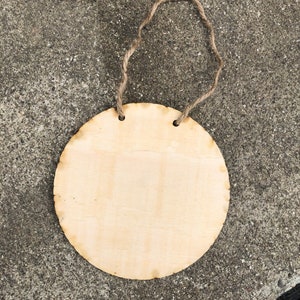May include: A round, unfinished wooden sign with a rope hanger. The sign is blank and ready to be decorated.