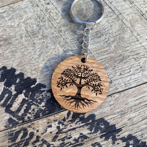 May include: A wooden keychain with a circular design featuring a tree of life with intricate roots and branches. The keychain is attached to a silver metal ring.