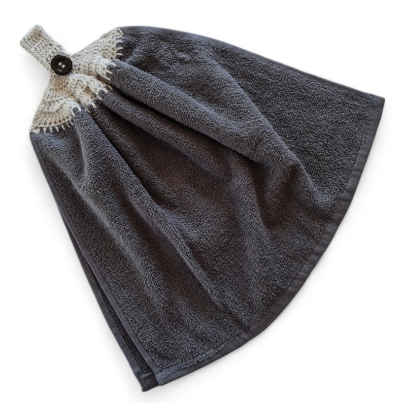 May include: A dark gray hand towel with a crocheted top and button closure. The towel is folded and has a textured surface. The crocheted top is light beige with a decorative stitch.