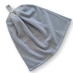 May include: A light blue hanging kitchen towel with a textured, ribbed design. The top features a crocheted section with a button closure for hanging. The towel is made of a soft, absorbent material, perfect for drying hands or dishes.
