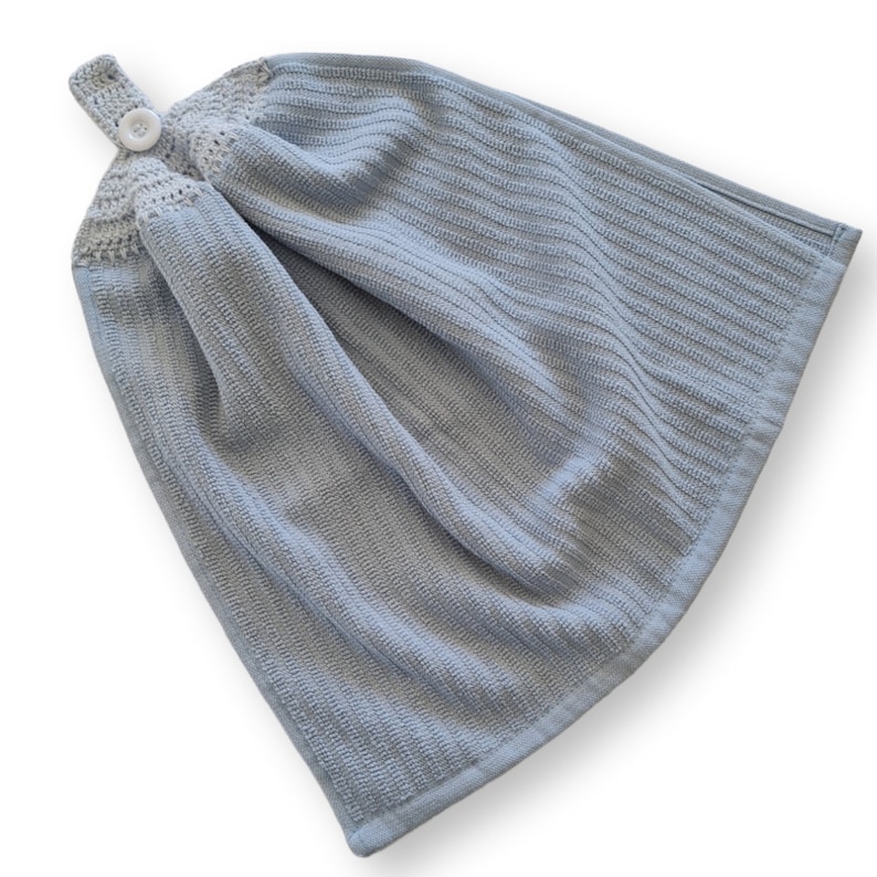May include: A light blue hanging kitchen towel with a textured, ribbed design. The top features a crocheted section with a button closure for hanging. The towel is made of a soft, absorbent material, perfect for drying hands or dishes.