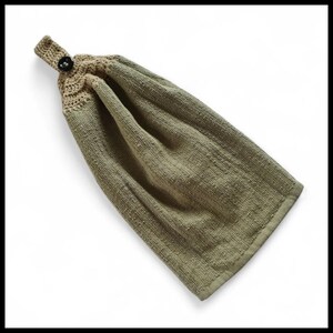 May include: An olive green hanging kitchen towel with a crocheted top section in a lighter tan colour. A dark button secures the loop for hanging. The towel has a textured appearance.
