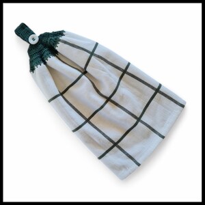 May include: White kitchen towel with a dark green grid pattern. The top is crocheted in dark green and has a white button for hanging. The towel is folded, displaying the grid design. A practical and decorative kitchen accessory.