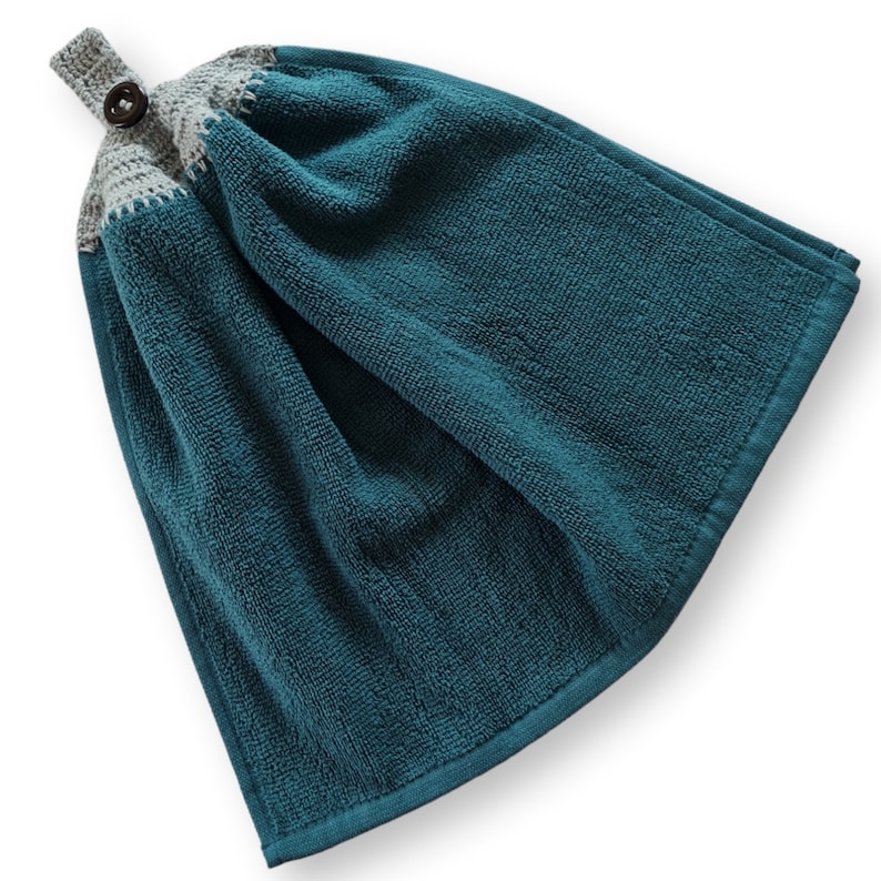 May include: Teal hanging kitchen towel with a gray crocheted top and a wooden button closure. The towel is made of a soft, absorbent material and has a loop for hanging. The towel is approximately 18 inches long and 12 inches wide.