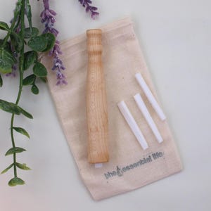 May include: A wooden toothbrush handle with four white replacement brush heads in a small, natural cotton drawstring bag. The bag has the text "the essential life" printed on it.