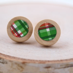 May include: Two round wooden stud earrings with a plaid pattern in green, red, and white. The earrings have a light brown wooden border and are set against a light wood background.
