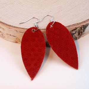May include: A pair of red leather earrings with a textured surface. The earrings are shaped like teardrops and have silver hooks.