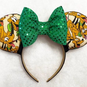 Puede incluir: Diadema con lazo de lentejuelas verdes y un diseño de tela de Pluto de Mickey Mouse Clubhouse de Disney.