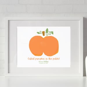 May include: A framed print with an orange pumpkin illustration and green vines. The text "Cutest pumpkin in the patch!" is written in orange script below the pumpkin. The print is in a white frame.