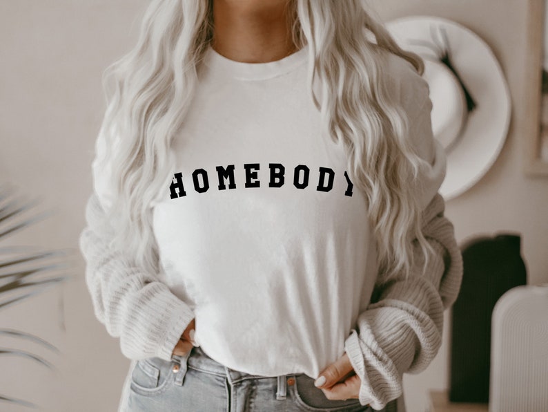 May include: White long-sleeve shirt with the text "HOMEBODY" printed in black.