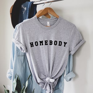 May include: A gray t-shirt with the text "HOMEBODY" printed in black letters.