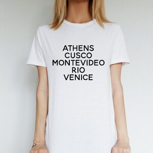 May include: White t-shirt with black text that reads "Athens, Cusco, Montevideo, Rio, Venice".