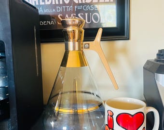 Elegante caraffa in vetro vintage con finiture dorate e manico beige.