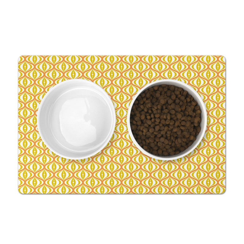 Pet food mat with a mid-century modern pattern design of yellow-gold, coral and white hourglass shapes